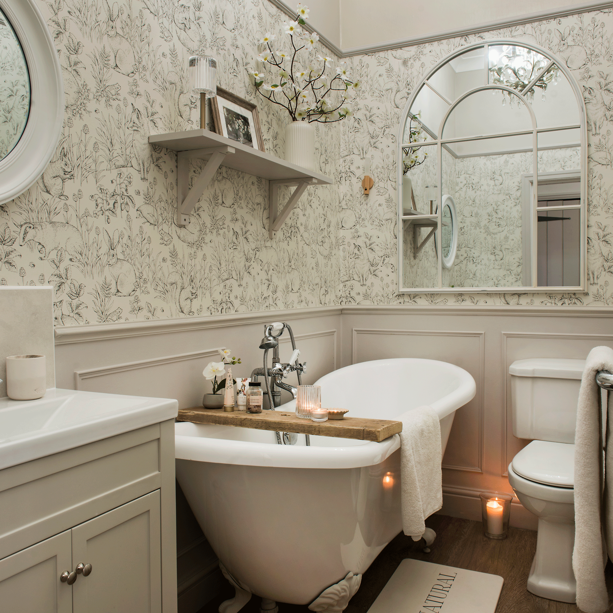 a classic bathroom with a freestanding bath tub wallpapered and panelled walls and a large arc mirror