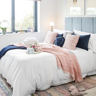 bed with blue headboard, white bedding and pink and blue cushions