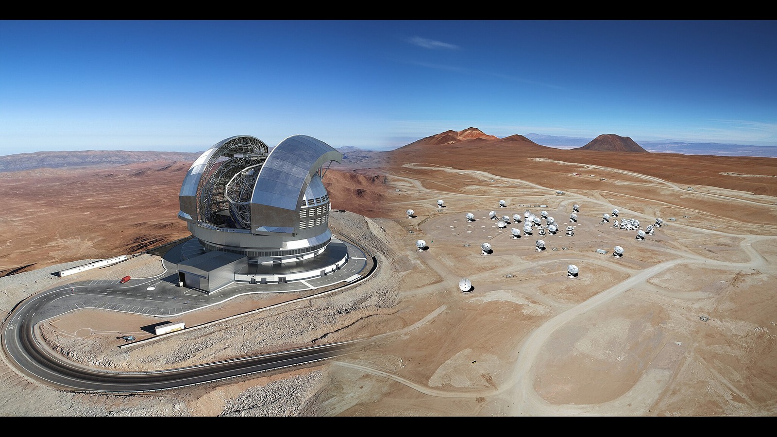 A large observatory sits on the hill next to an array of satellite dishes.