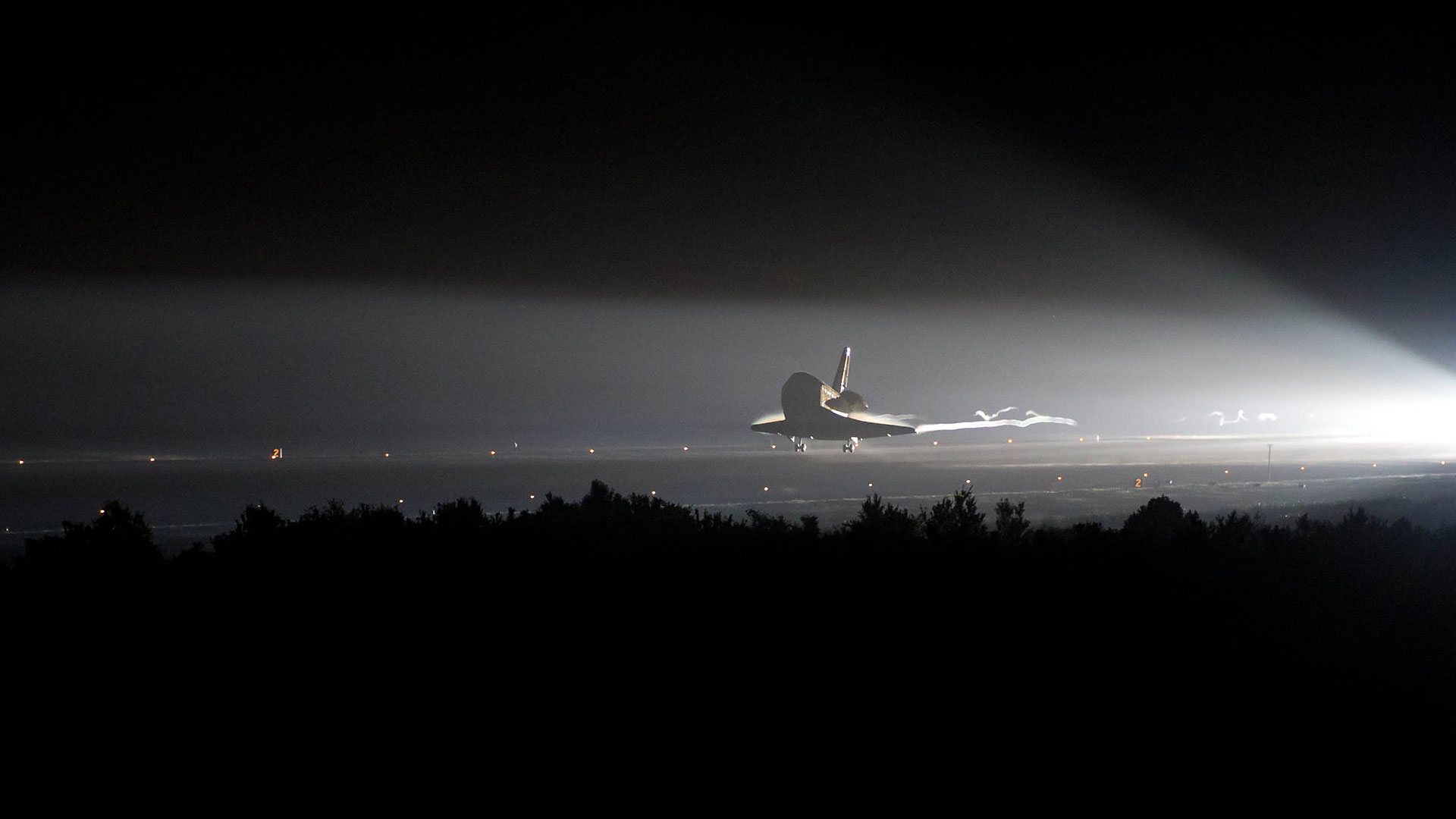 a winged spacecraft touches down in the dark of night, lit only by a spotlight