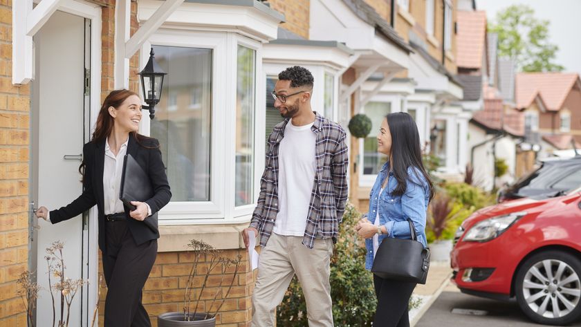 Estate agent with folder under her arm opening the front door to a terraced home to show man and woman around