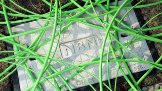 Green NBN fibre optic cable strewn across an NBN hole cover