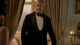 A tuxedo clad Hugh Bonneville stands in an upstairs room in Downton Abbey.