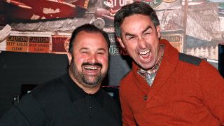 Getty image of Frank Fritz wearing black and Mike Wolfe wearing orange in an early American Pickers promo photo. Both are doing goofy faces.