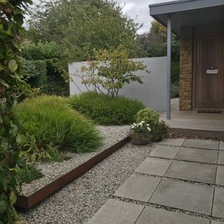 a low maintenance front garden, with slabs and gravel leading to the front door and shrubs and trees to the right