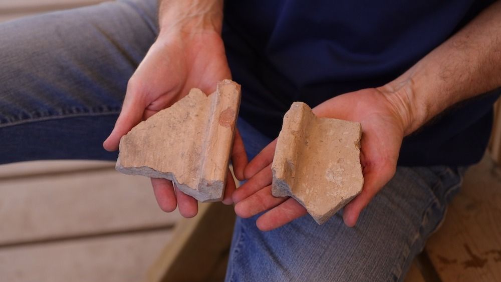 A man holds two ceramic tiles.