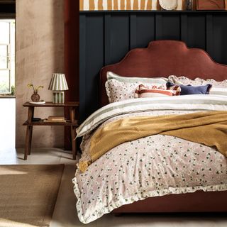 A bed with a curved fabric headboard and floral bed linen