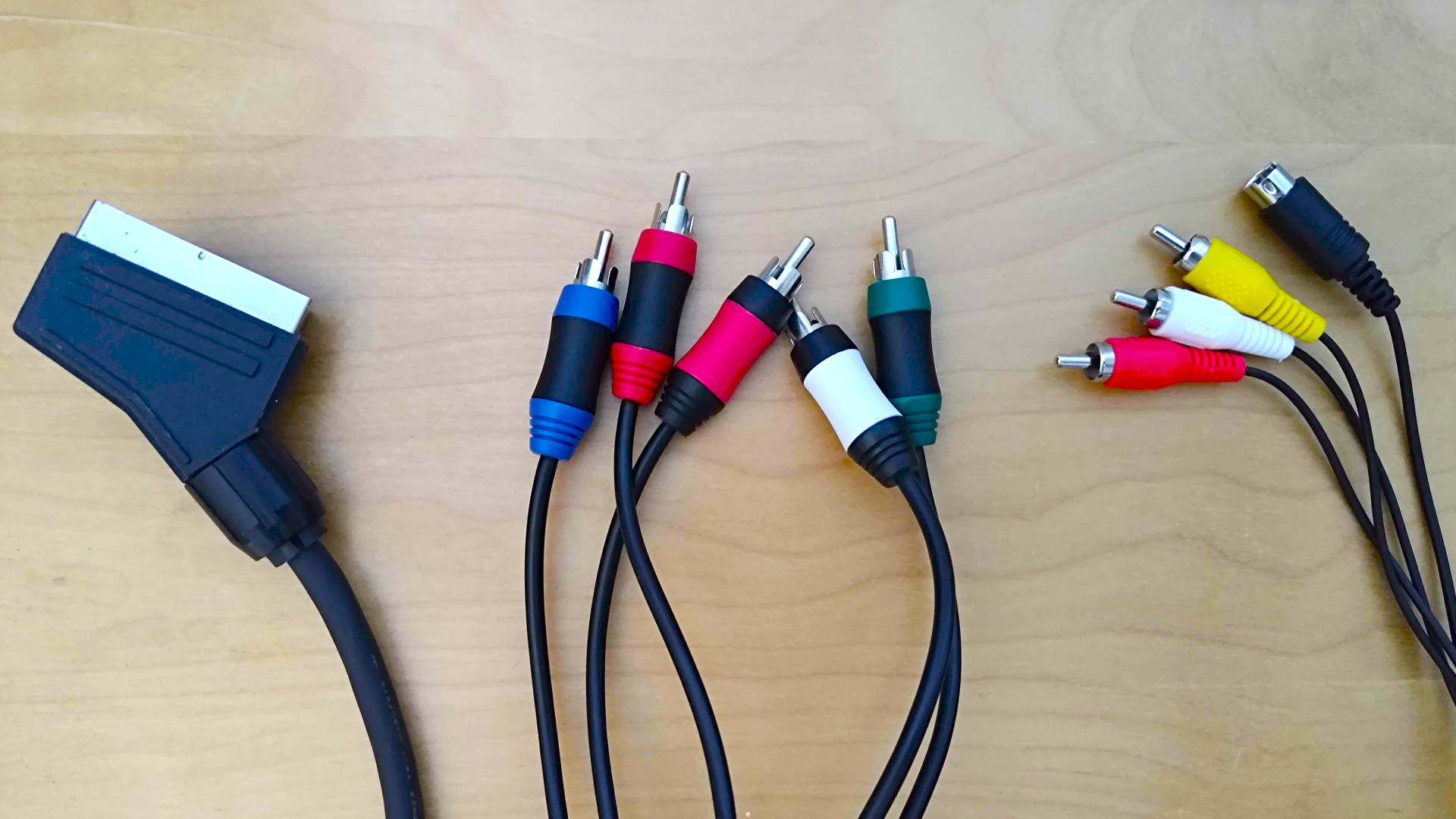 RGB SCART, component, and Composite/S-Video cables on woodgrain bench.