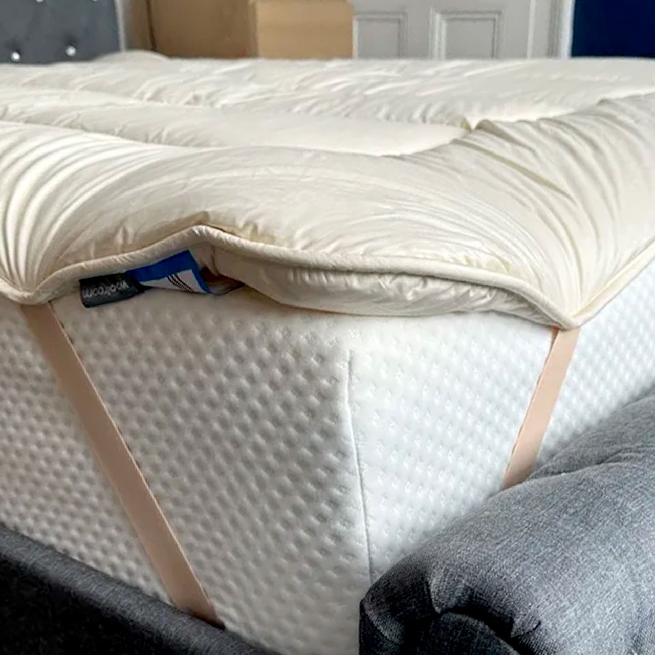 The corner of the Woolroom Deluxe Wool Mattress Topper showing its elasticated straps holding it in place on a mattress