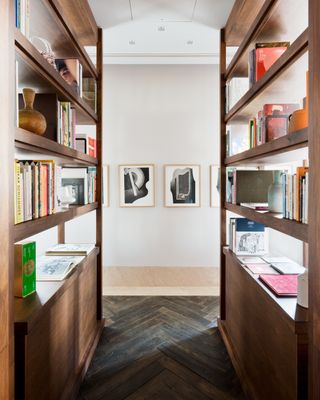 A view between two wooden bookshelves and a white wall with paintings on it.