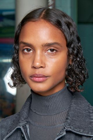 A model with a curly bob hairstyle and black turtleneck.