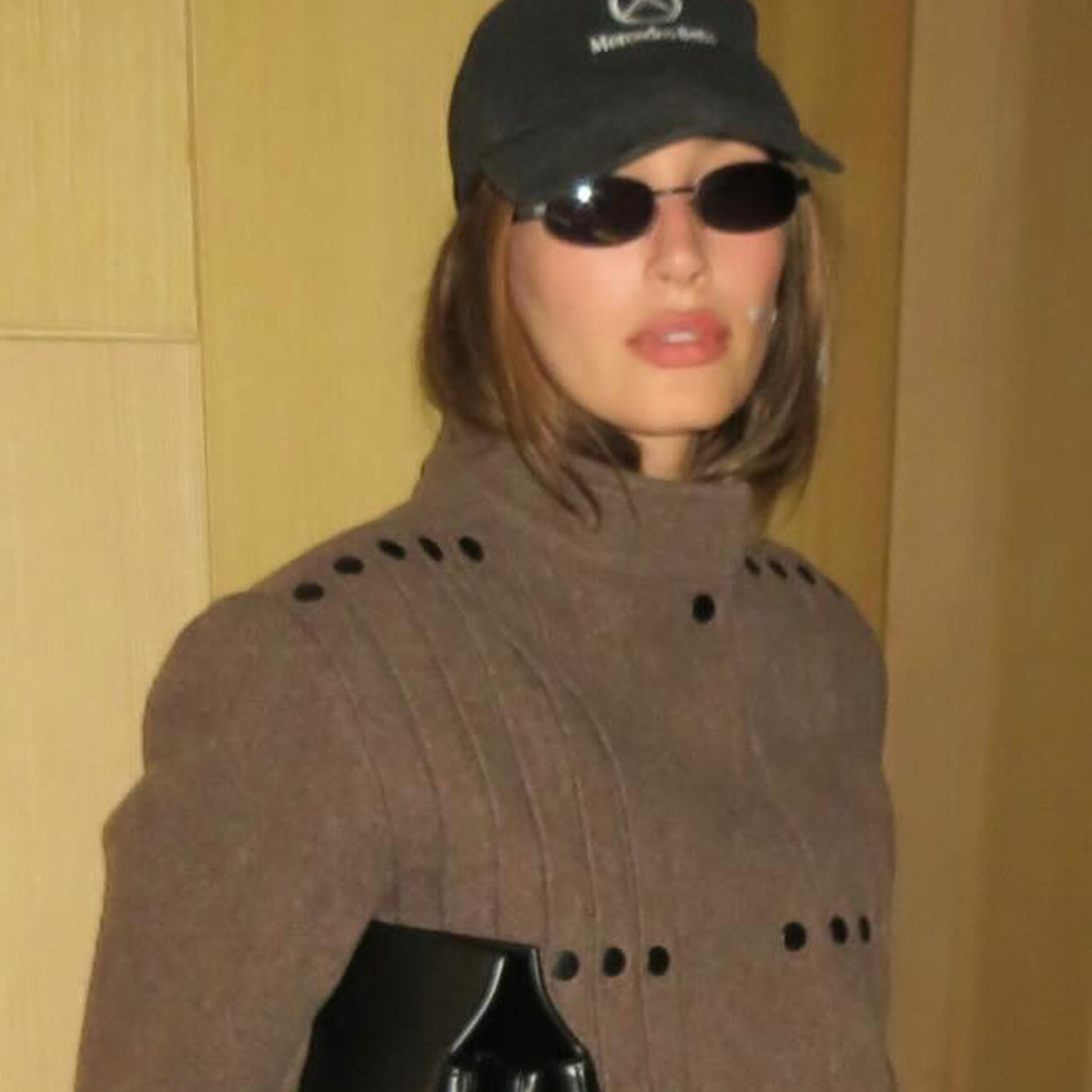 Hailey Bieber in Tokyo wearing a Mercedes baseball cap, brown jacket, and black leather pants.