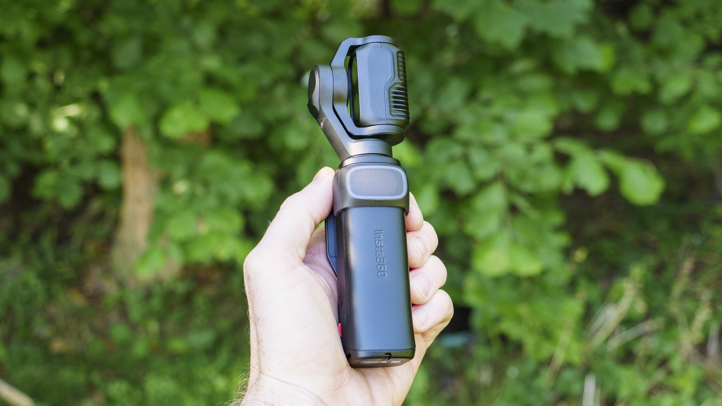 Insta360 Luna Ultra vlogging camera in person's hand, turned off, leafy background