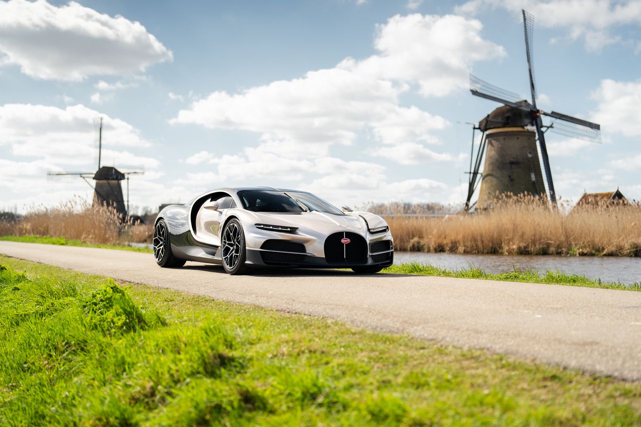 A Bugatti tourbillon in the netherlands, with two windmills behind it.