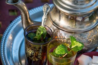 A silver tea pot next to two small glasses of mint tea on a table in Morocco