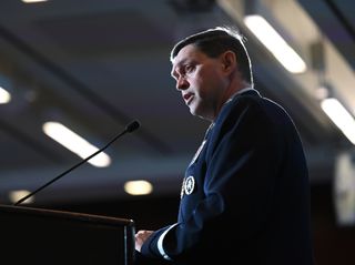 a man in a dark blue suit speaks into a microphone at a lectern