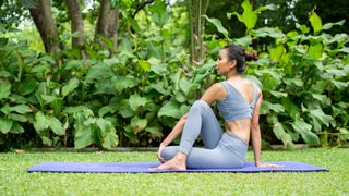 Woman performing a seated twist outdoors during yoga class on mat