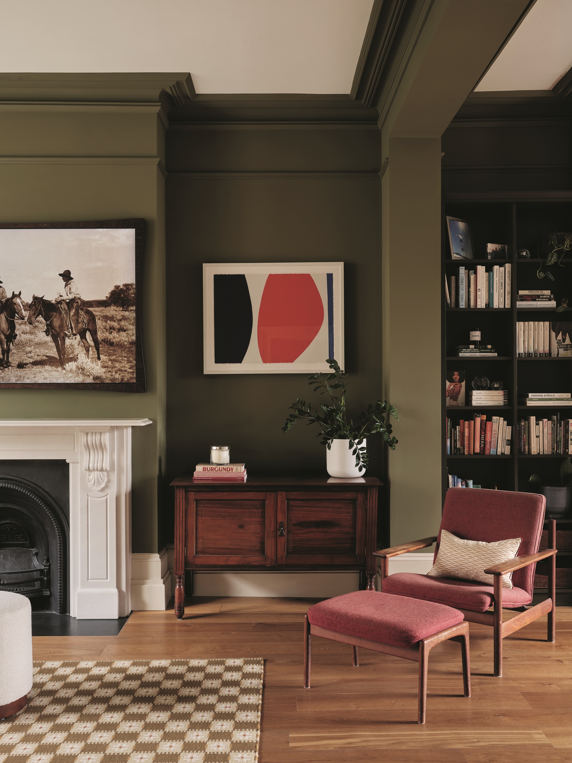 a green living room with a pink chair, and a wooden cabinet with bookshelves