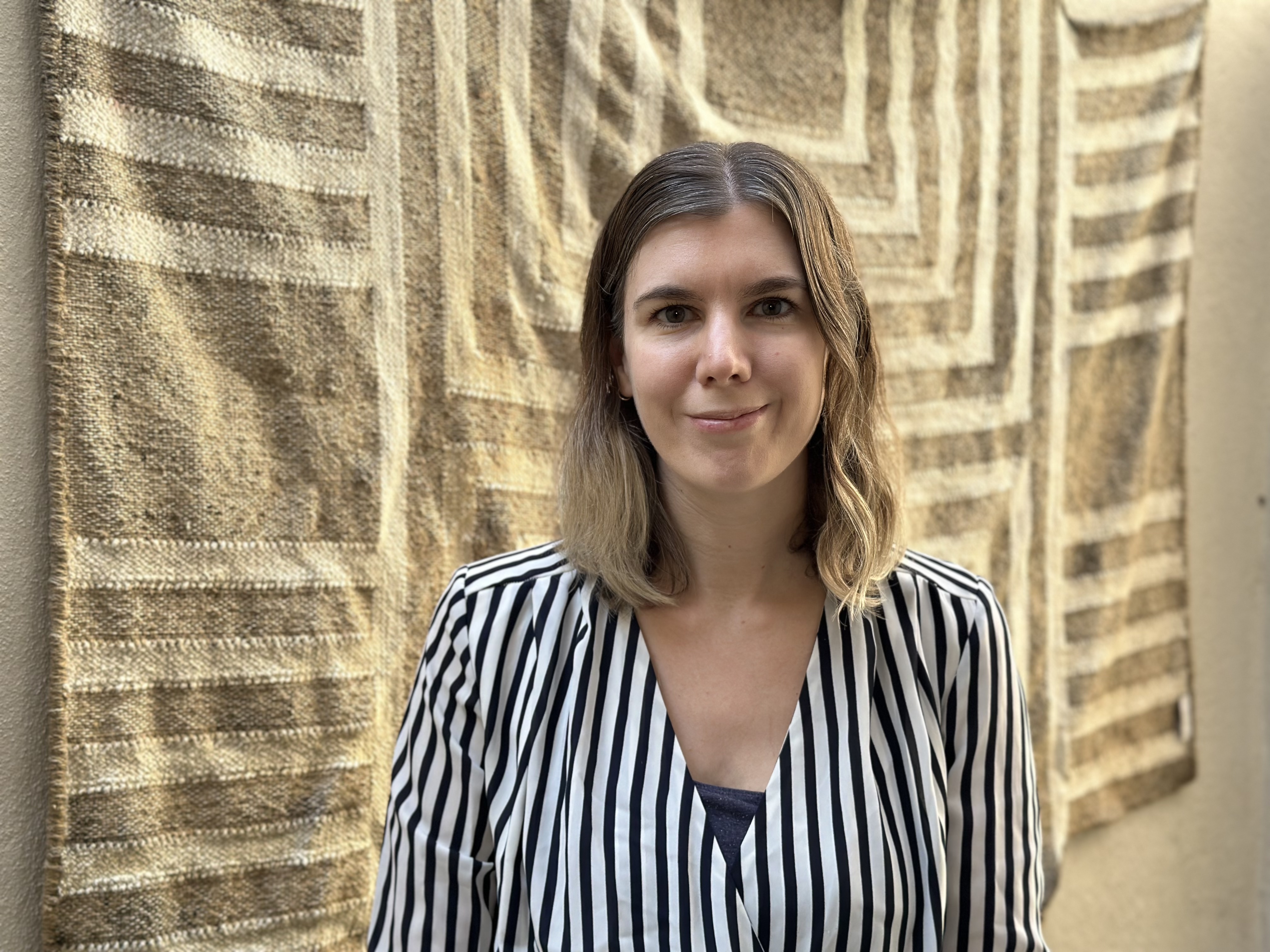 portrait of author Sarah Housley standing in front of textile wall hanging