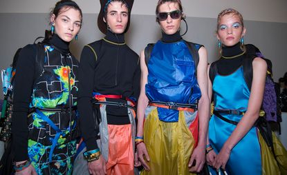 4 models stood together in a studio wearing brightly coloured clothing