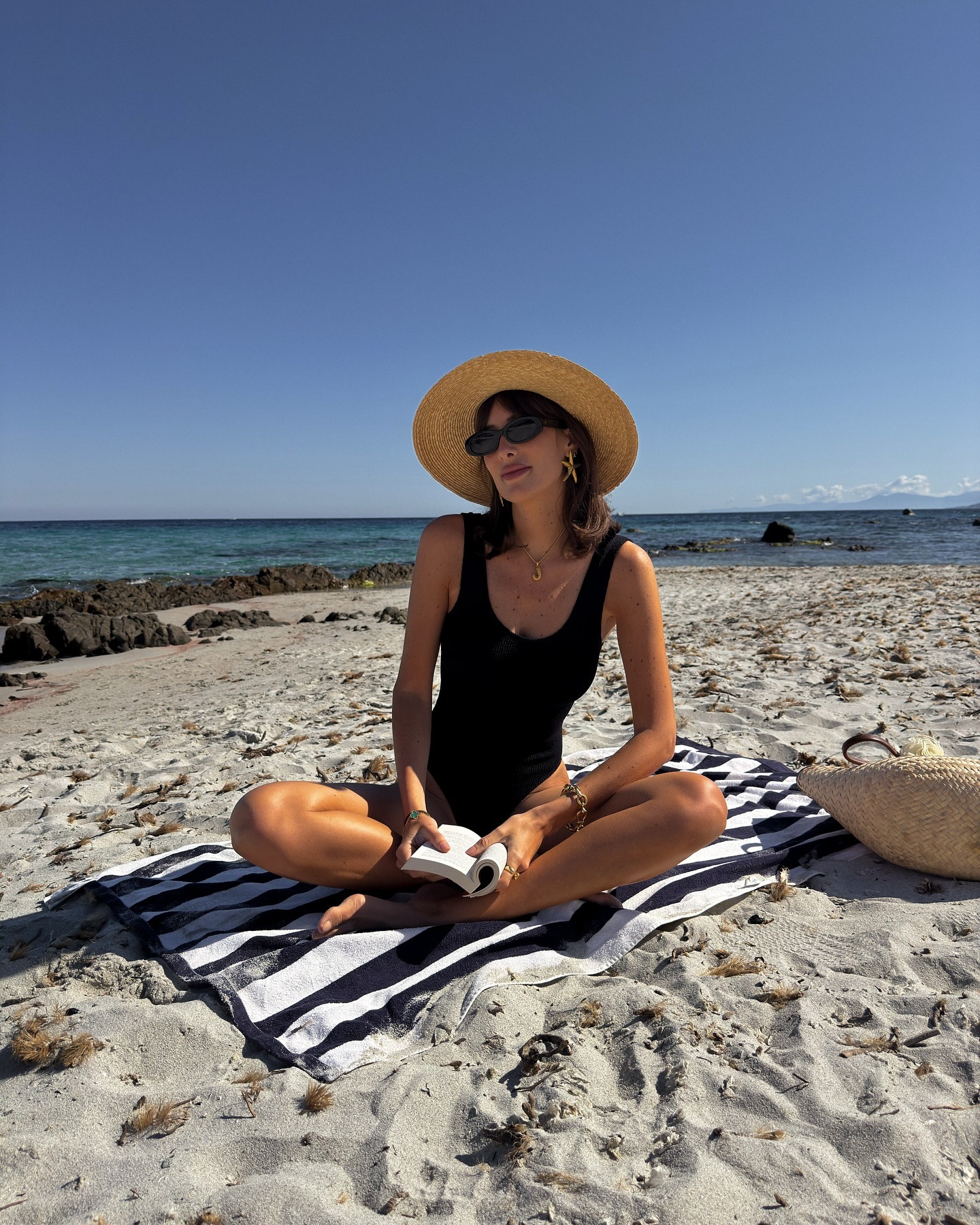 French woman wearing a black swimsuit and raffia hat on the beach.