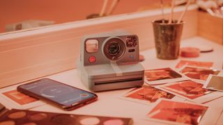 Polaroid Now Plus camera on desk in darkroom surrounded by Polaroid prints