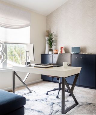 A white home office with white walls, a blue cabinet with plants and decor on it, a white desk with a computer and white mug on it and black legs, and a blue and white rug