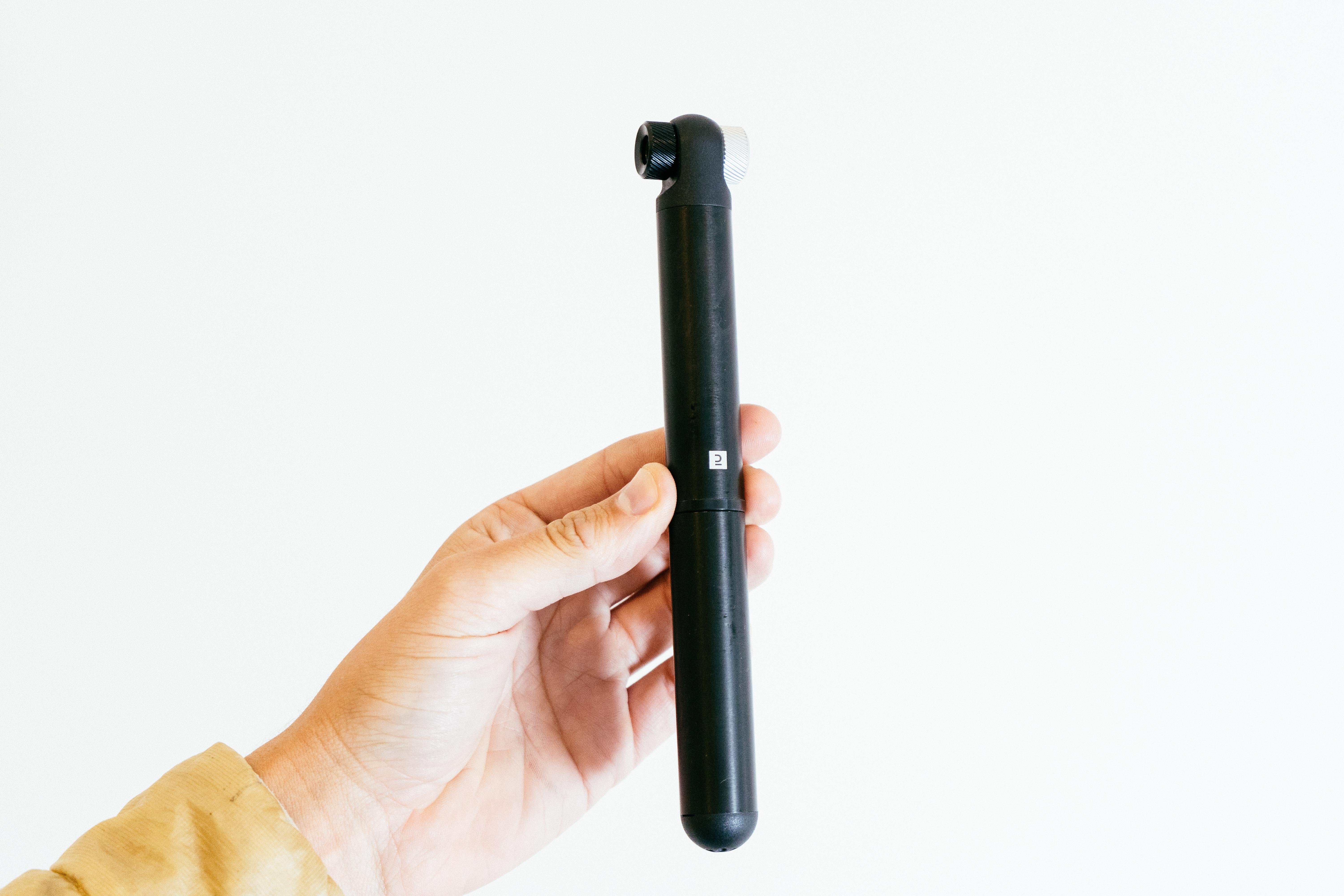 A black mini pump held vertically against a white wall