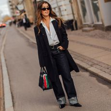 Fashion week attendee wearing sunglasses, button down shirt, black coat, cuffed jeans