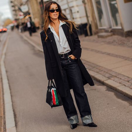 Fashion week attendee wearing sunglasses, button down shirt, black coat, cuffed jeans 