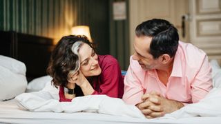 Woman and man lying on bed together smiling and talking, representing how to revive your sex life by taking things slowly
