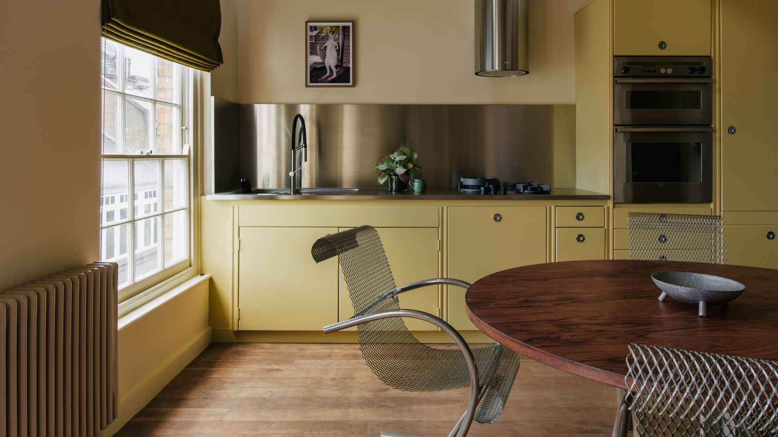 butter yellow kitchen with wooden floors, chrome backsplash and a chrome extractor hood with a wooden round table and chrome chairs