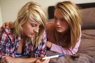 Two teen girls examine a pregnancy test result.