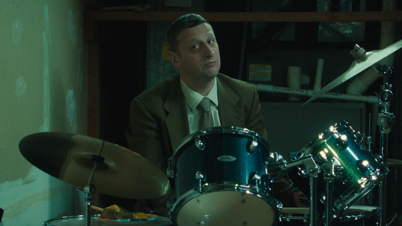 Tim Robinson's Craig sitting behind drum set in Friendship