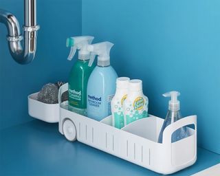 An under sink sliding storage caddy with household cleaning products and U-pipe