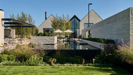 An outdoor garden with a pool, an outdoor living room, a green lawn, tall feathered purple flowers, and ground cover