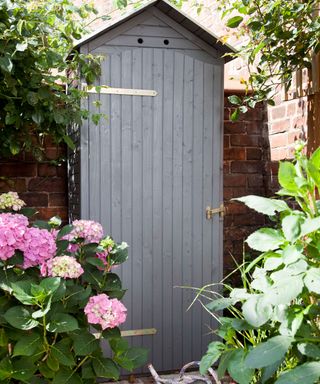 A tall and narrow garden shed painting in grey.