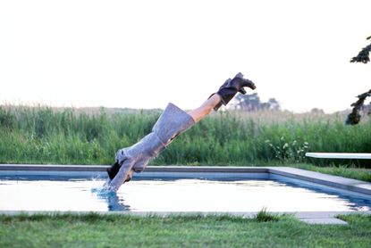 Model Stella Tennant, diving into pool, wearing a wool jacket and wrap-around skirt by ICB, and boots