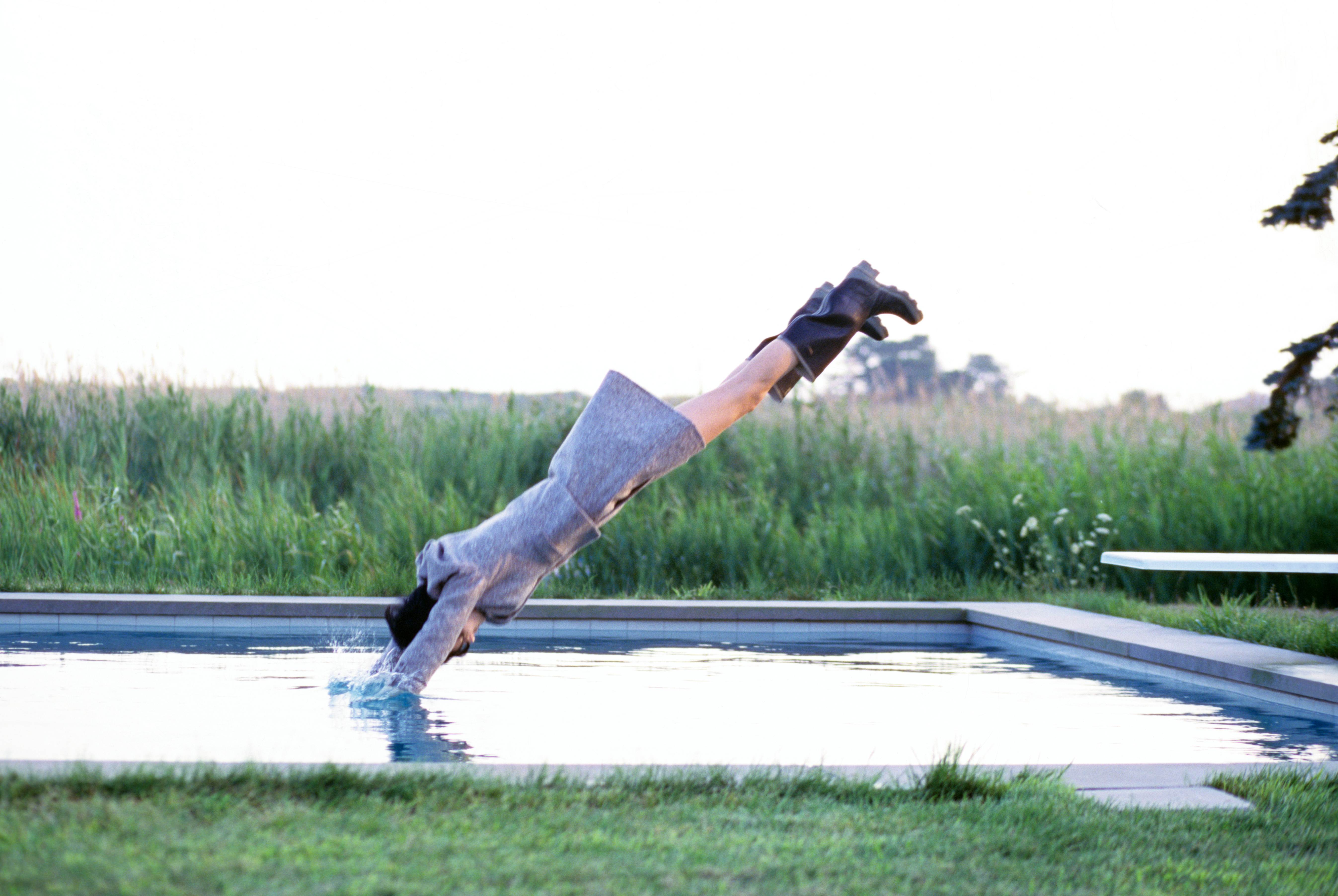 Model Stella Tennant, diving into pool, wearing a wool jacket and wrap-around skirt by ICB, and boots
