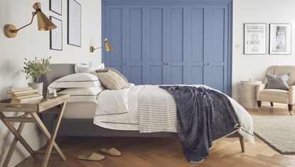 Bedroom with blue walls and wooden shelving and wall panelling above a bed dressed in blue linen bedding