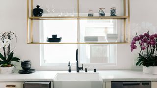 Kitchen shelving in gold above a sink in a white kitchen