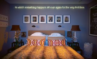Blue bedroom with double bed and "in Which Something Happens All Over Again for the Very First Time" sign on the wall