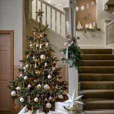 A decorated Christmas tree with presents at the bottom of a staircase