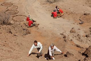 National Geographic Explorers-in-Residence Louise Leakey (left) and Meave Leakey search the slope in northern Kenya where KNM-ER 60000 was discovered while, in the background, members of the field crew screen the surface sediment hoping to find additional fragments of this fossil.