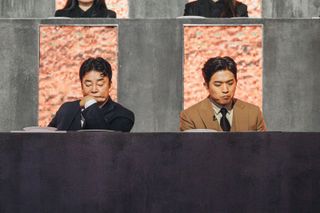 Judges Paik Jong-won and Anh Sung-jae consider a dish while sitting at an elevated table, in Culinary Class Wars