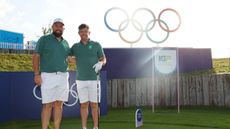 Shane Lowry and Rory McIlroy pose on a tee box with the Olympic rings in the background