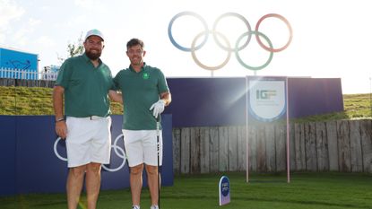 Shane Lowry and Rory McIlroy pose on a tee box with the Olympic rings in the background