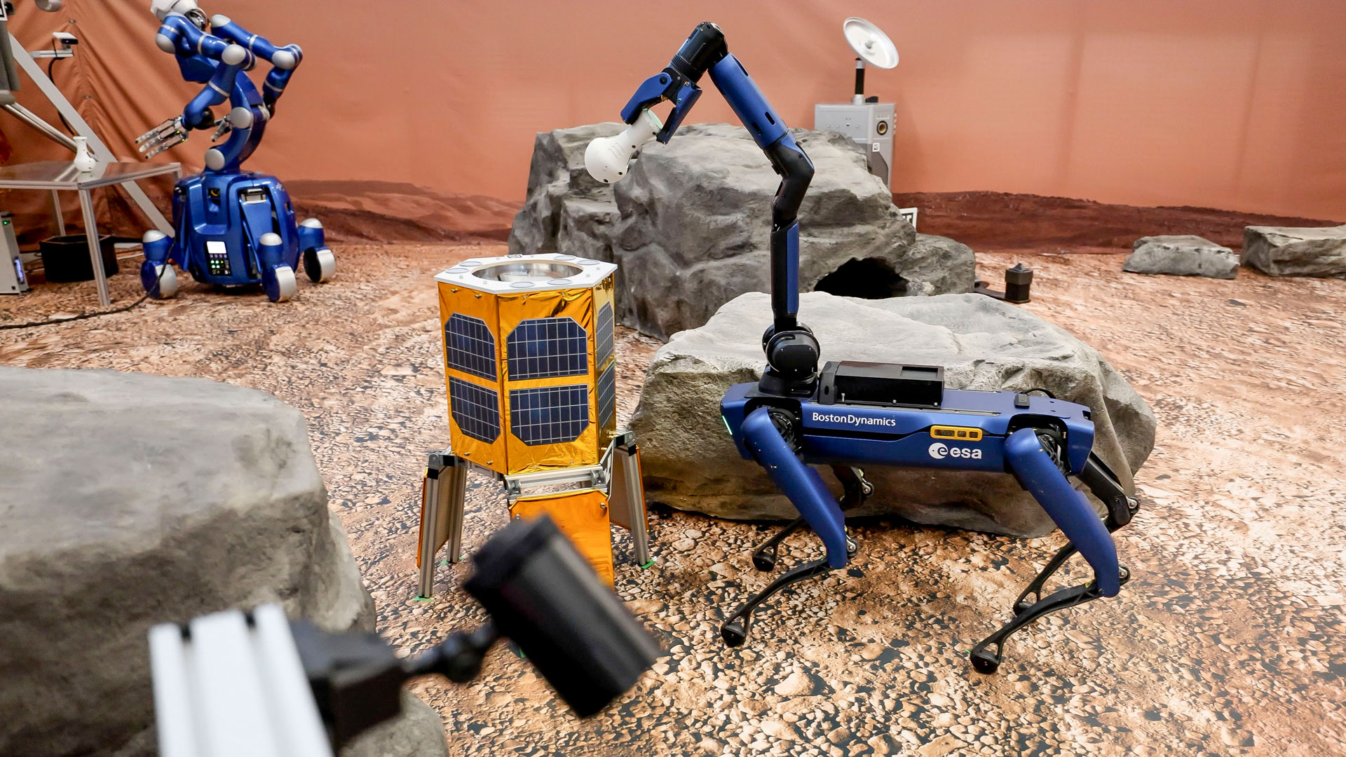 A four-legged robot walks over to a small metal cube with solar panels