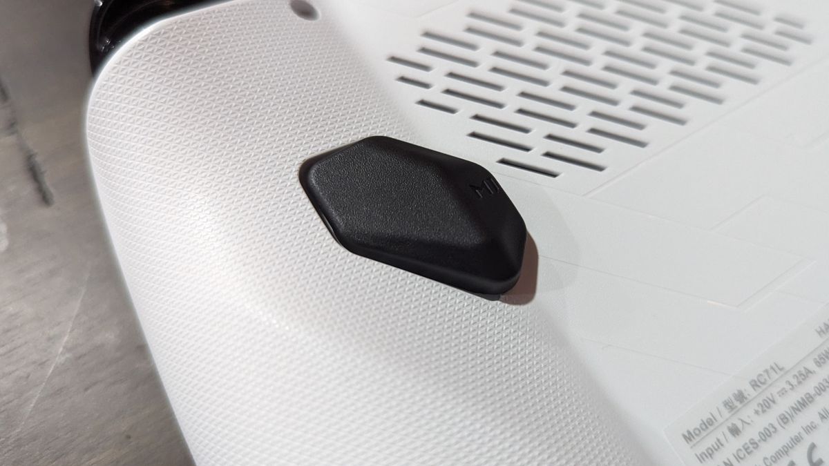 Asus ROG Ally Z1 on a brown table, highlighting the additional button and vents on the back of the device.