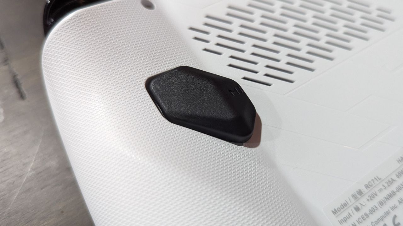 Asus ROG Ally Z1 on a brown table, highlighting the additional button and vents on the back of the device.